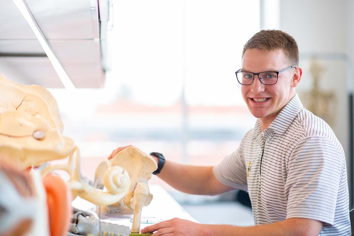 一个穿着运动衫的年轻人坐在办公桌前，手里拿着一个髋骨模型.